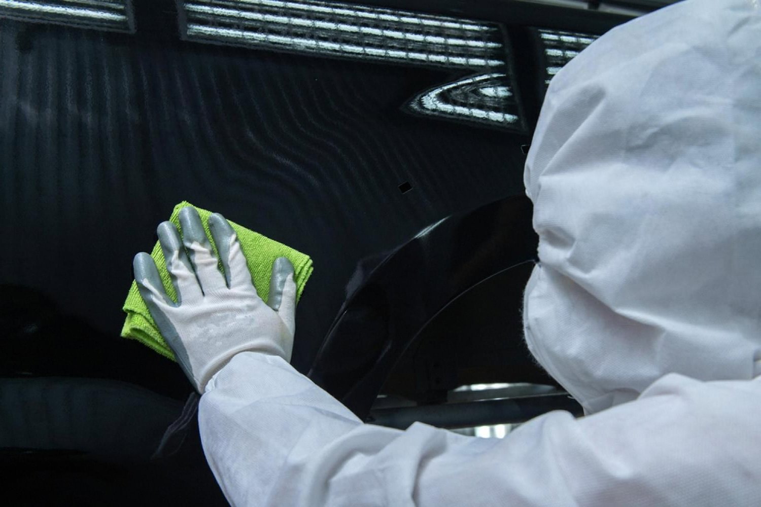 Worker in protective suit wiping down a black car panel after paint protection application
