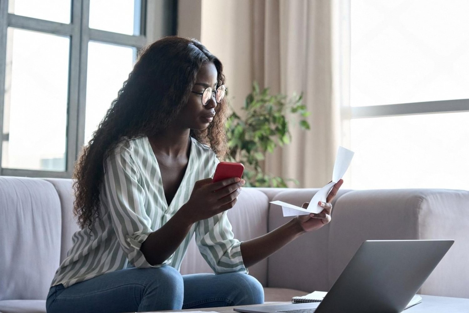 Young woman on a sofa checking a home insurance bill on her phone at home in Dubai